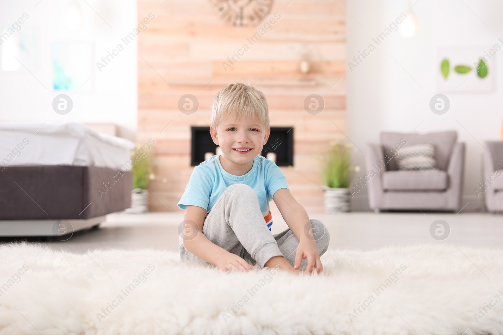 Photo of Cute little boy sitting on fur rug at home
