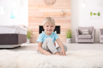 Photo of Cute little boy sitting on fur rug at home