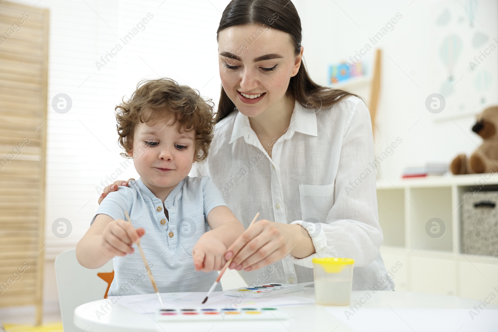 Photo of Mother and her little son painting with watercolor at home