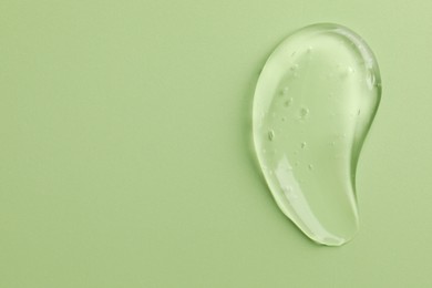 Smear of clear cosmetic gel on light green background, top view. Space for text