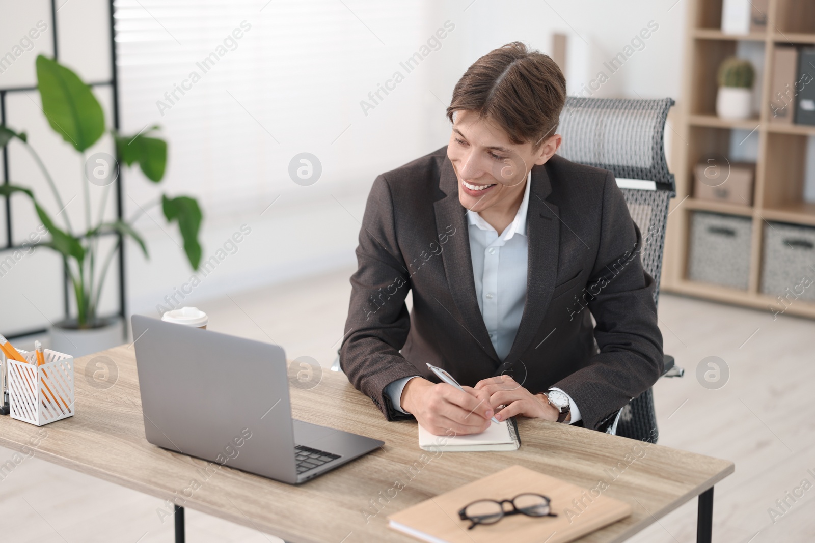 Photo of Man taking notes during webinar at wooden table indoors