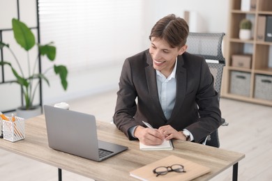 Photo of Man taking notes during webinar at wooden table indoors