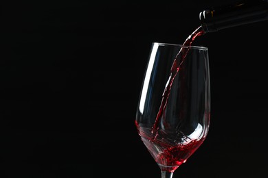 Photo of Pouring red wine into glass against black background, closeup. Space for text