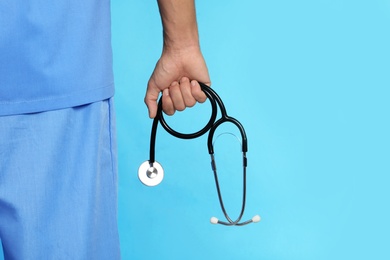 Male doctor holding stethoscope on color background, closeup with space for text. Medical object
