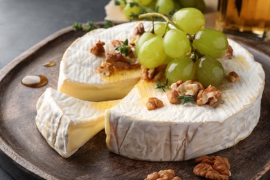Photo of Brie cheese served with grapes, walnuts and honey on grey table, closeup