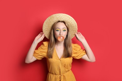 Photo of Fashionable young woman with bright makeup blowing bubblegum on red background