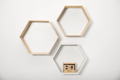 Photo of Honeycomb shaped shelves with wooden block calendar on white wall