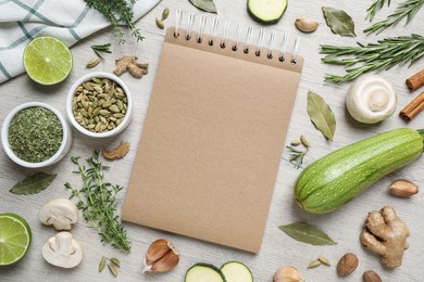 Open recipe book and different ingredients on white wooden table, flat lay. Space for text