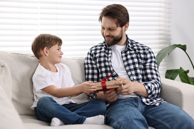 Photo of Happy Father's day. Son giving gift box to his dad on sofa at home