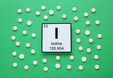 Photo of Card with iodine element and pills on green background, flat lay