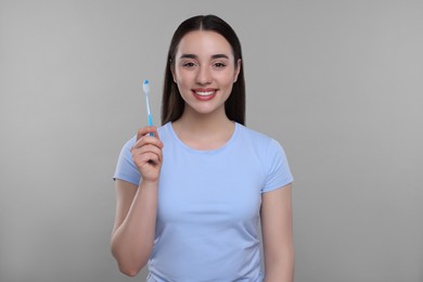 Photo of Happy young woman holding plastic toothbrush on light grey background