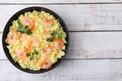 Photo of Delicious risotto with shrimps and parsley in bowl on white wooden table, top view. Space for text