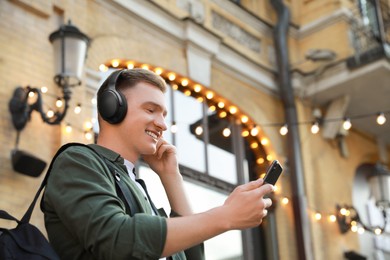Photo of Smiling man in headphones using smartphone outdoors. Space for text