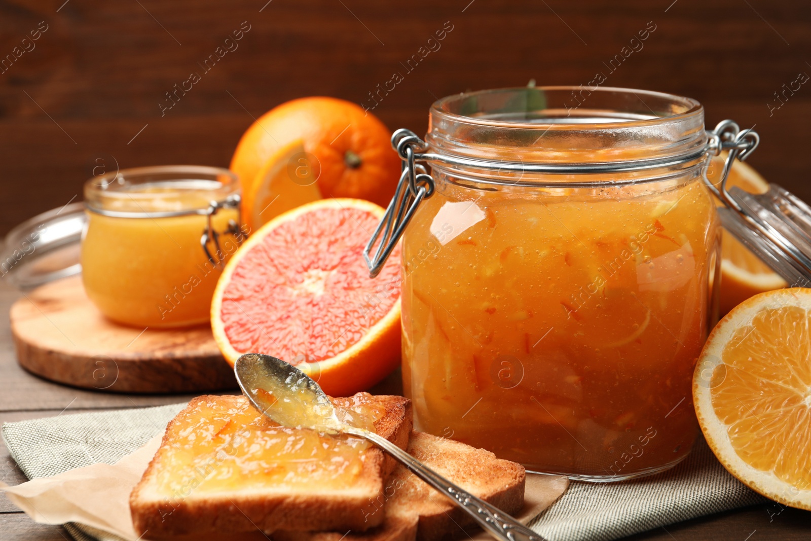 Photo of Delicious orange marmalade in jar, fresh fruits and toasts on table