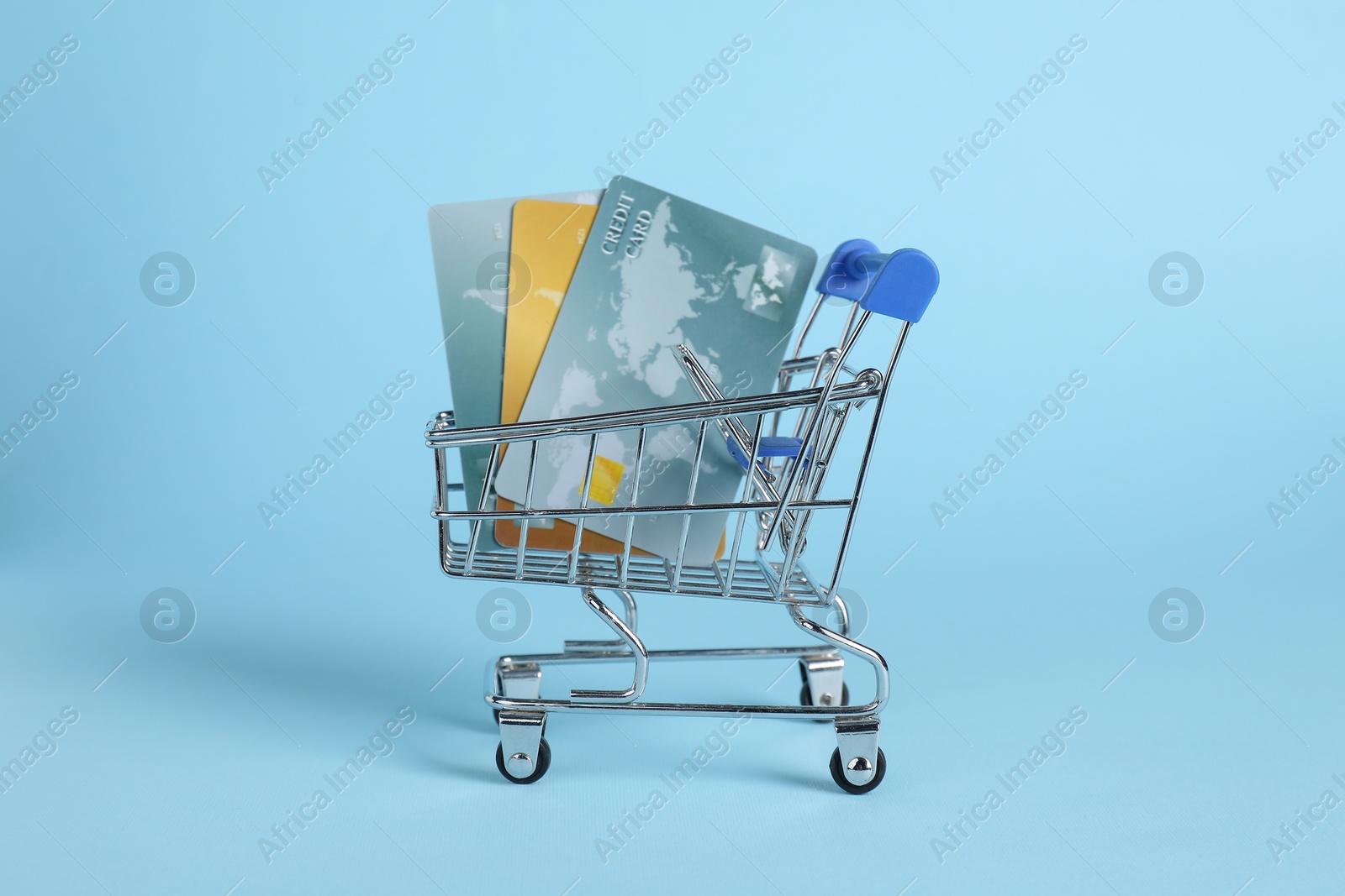 Photo of Small metal shopping cart with credit cards on light blue background