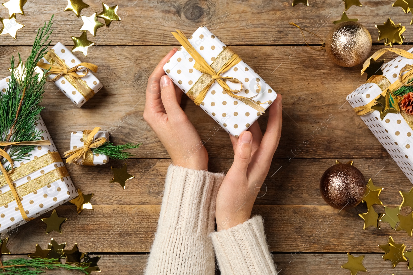 Photo of Woman holding Christmas gift box with golden bow at wooden table, top view