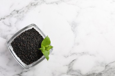 Photo of Black sesame seeds and green leaf in glass bowl on white marble table, top view. Space for text