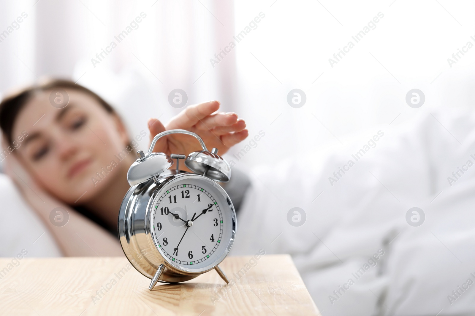 Photo of Young woman turning off alarm clock at home in morning, focus on hand. Space for text