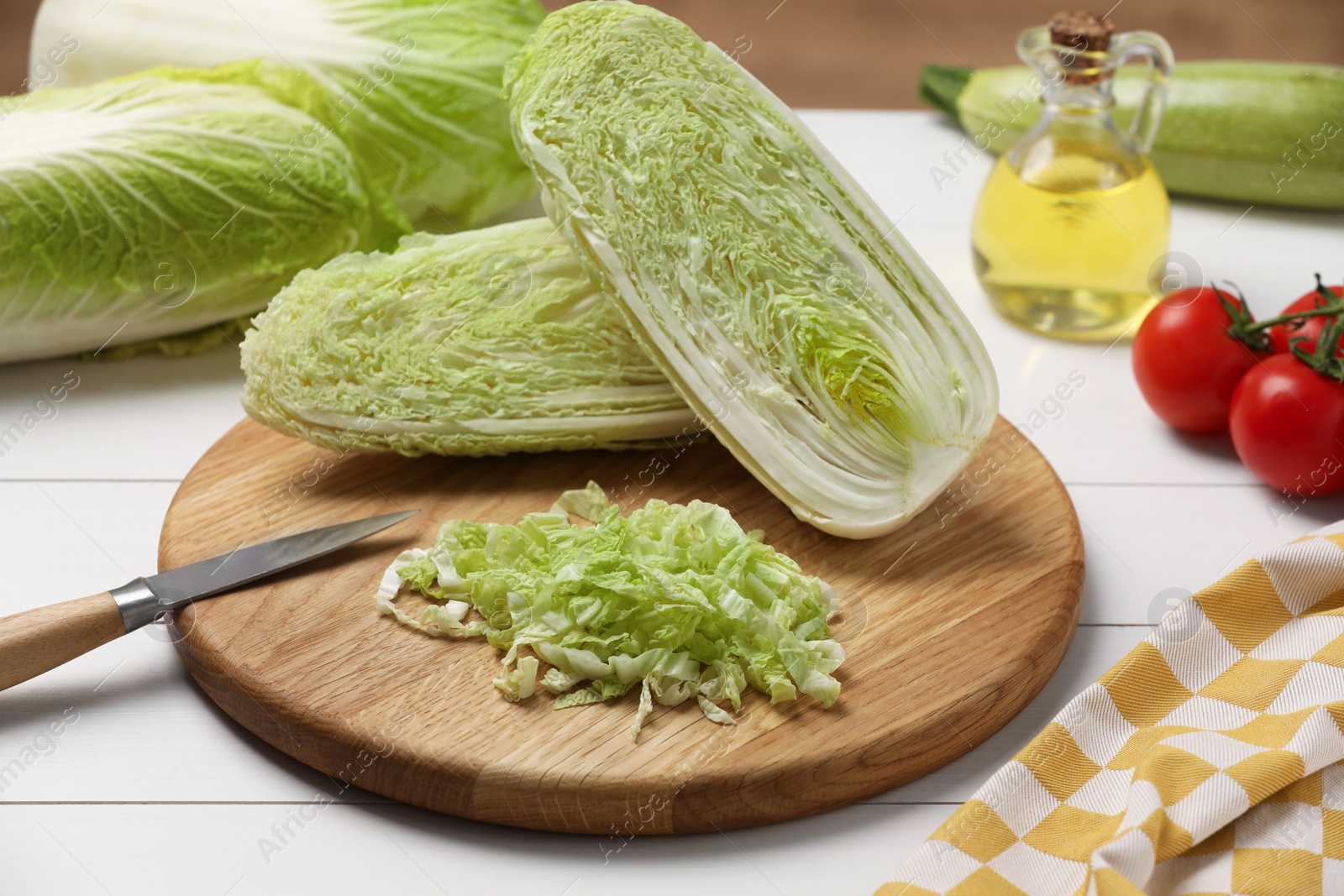 Photo of Fresh Chinese cabbages, knife, tomatoes and oil on white wooden table