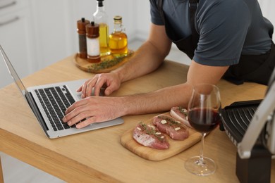 Man making dinner while watching online cooking course via laptop in kitchen, closeup