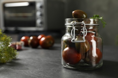 Photo of Pickling jar with fresh tomatoes on black kitchen table, closeup. Space for text