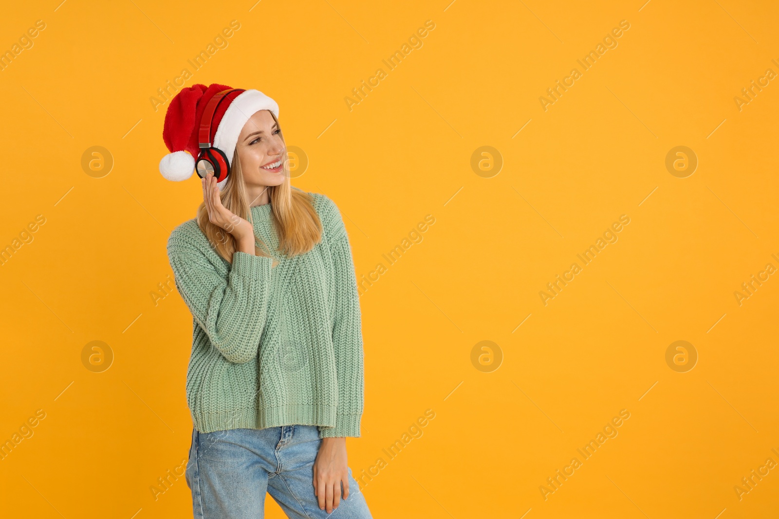 Photo of Happy woman with headphones on yellow background, space for text. Christmas music