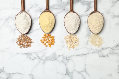 Spoons with different types of flour and ingredients on marble background, top view. Space for text