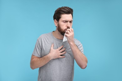 Sick man with tissue coughing on light blue background