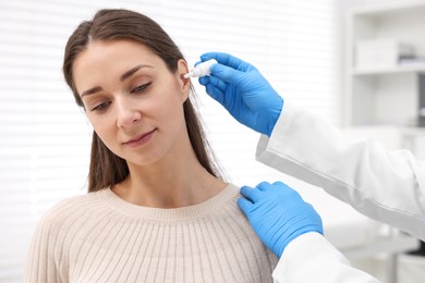 Doctor applying medical drops into woman's ear indoors