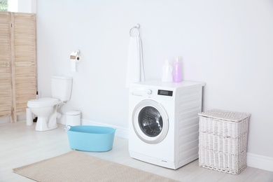 Photo of Modern washing machine in light bathroom interior