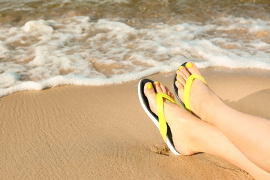 Photo of Closeup of woman with flip flops on sand near sea, space for text. Beach accessories