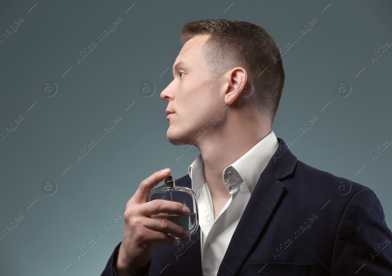 Photo of Handsome man in suit using perfume on dark background