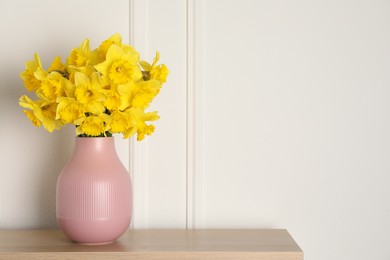 Beautiful daffodils in vase on table near white wall indoors, space for text