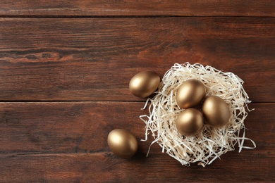 Nest with golden eggs on wooden background, top view. Space for text