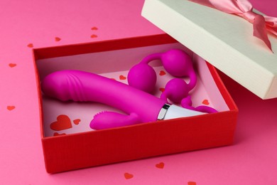 Photo of Gift box with sex toys on pink background, closeup