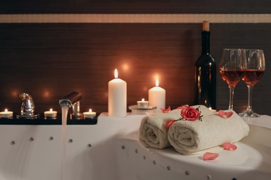 Photo of Glasses of wine, towels, candles and rose on tub in bathroom. Romantic atmosphere