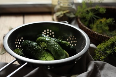 Photo of Fresh cucumbers in colander and other ingredients prepared for canning on wooden table, closeup