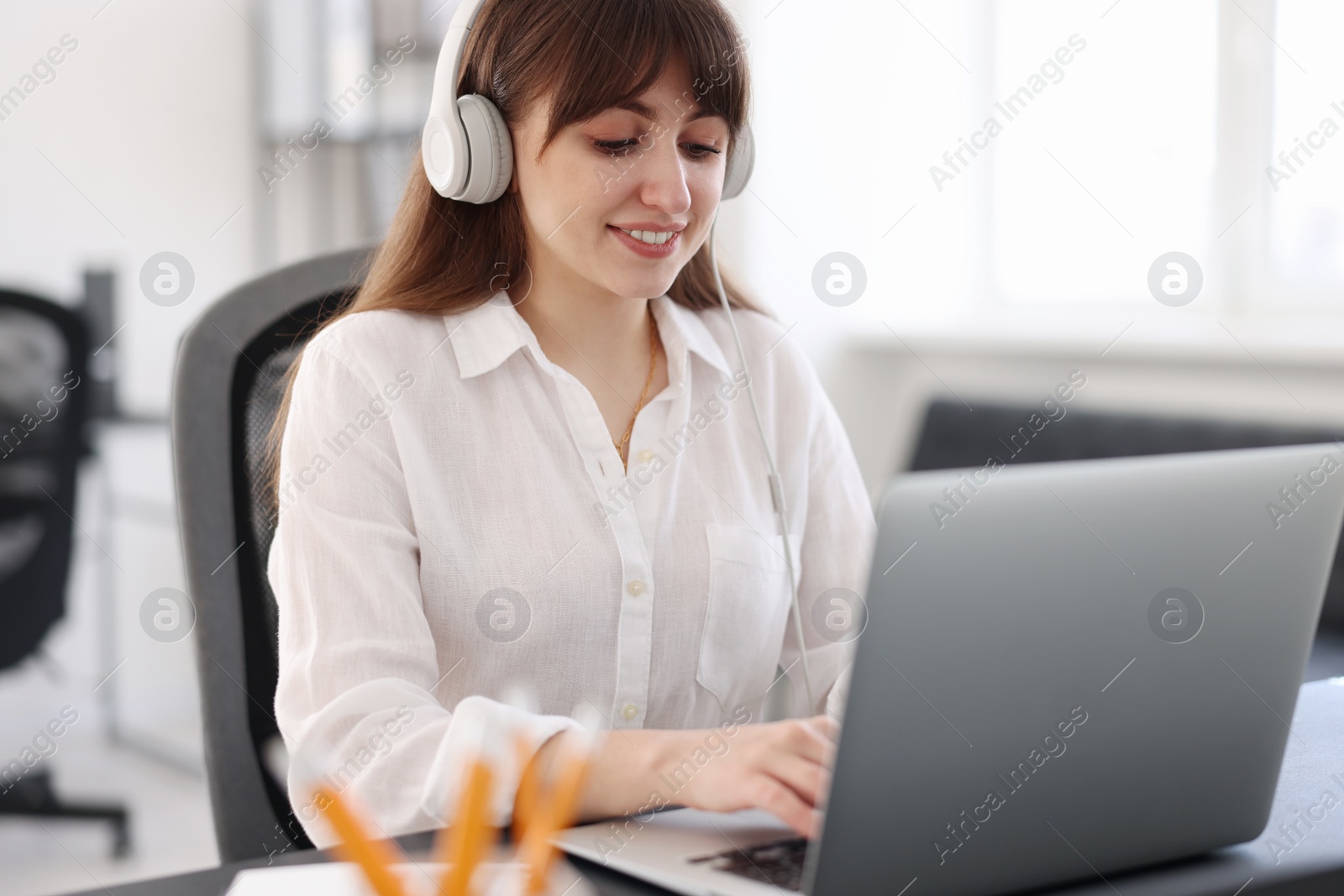 Photo of Woman in headphones watching webinar at table in office