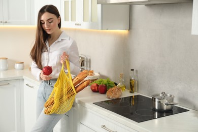 Photo of Woman with string bag of baguettes and apple in kitchen