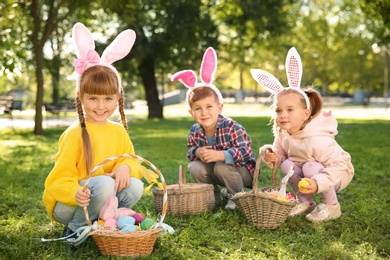 Photo of Cute little children hunting eggs in park. Easter tradition