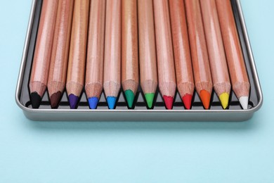 Photo of Colorful pastel pencils in box on light blue background, closeup. Drawing supplies