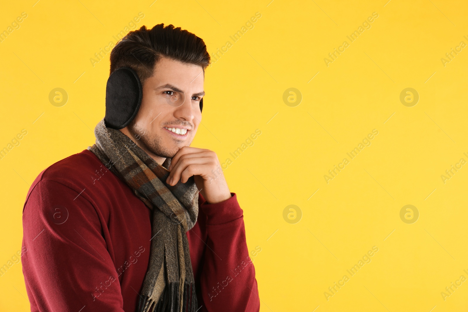 Photo of Man wearing stylish earmuffs and scarf on yellow background. Space for text