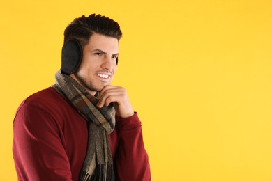 Man wearing stylish earmuffs and scarf on yellow background. Space for text