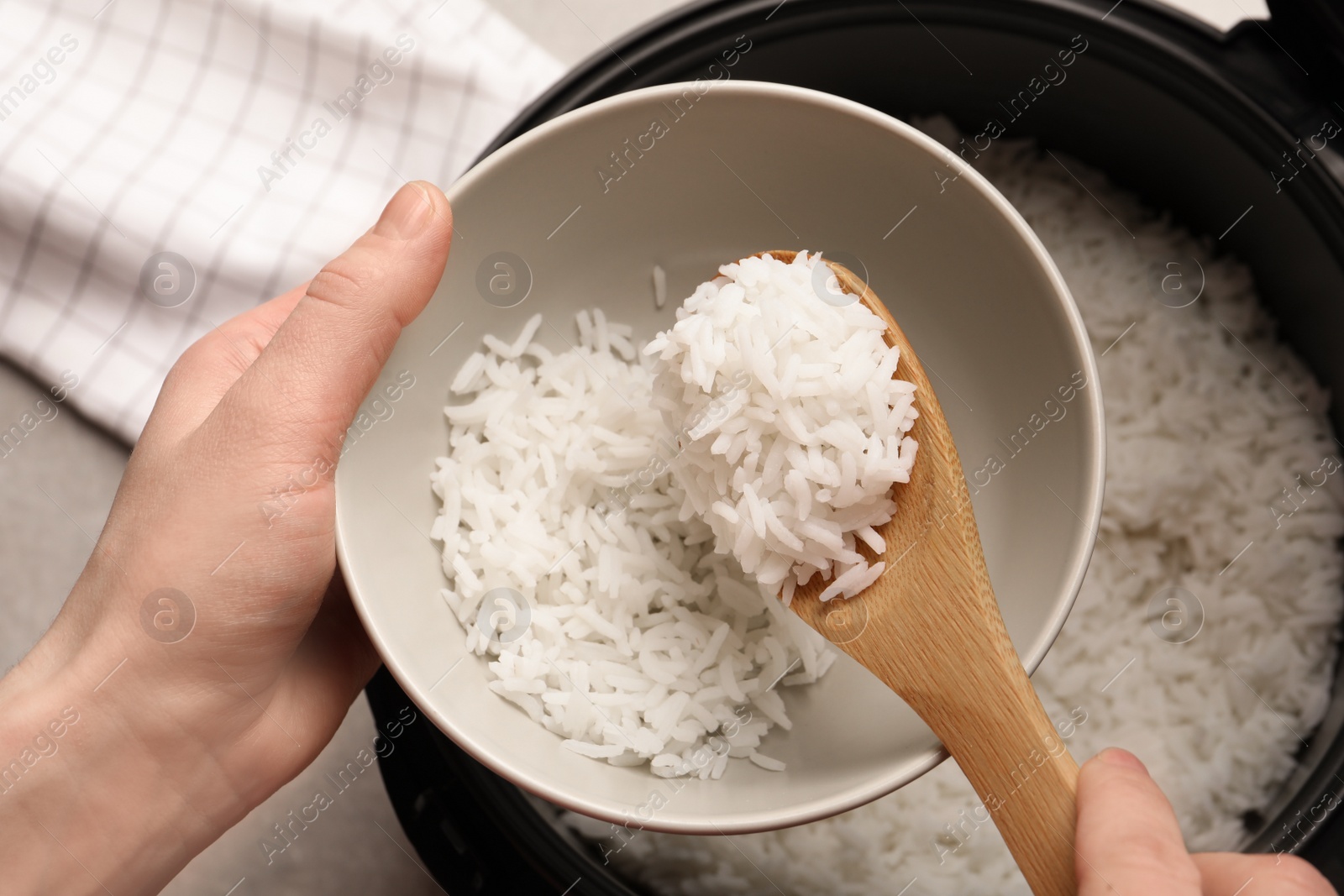 Photo of Woman putting rice into bowl from cooker in kitchen, top view