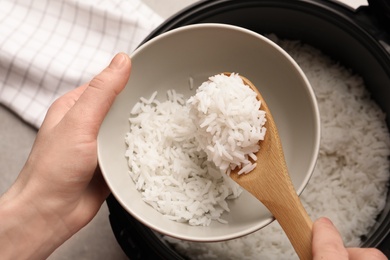 Photo of Woman putting rice into bowl from cooker in kitchen, top view