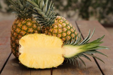 Whole and cut ripe pineapples on wooden table, closeup