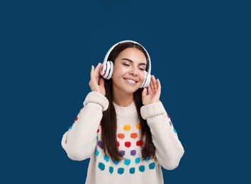 Young woman listening to music with headphones on dark blue background