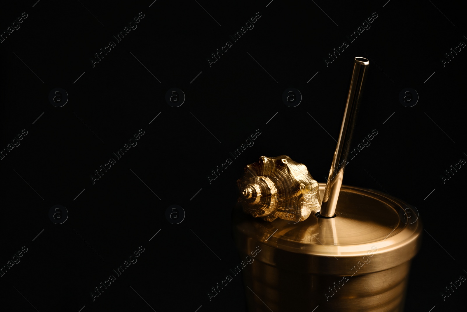 Photo of Gold cup with seashell on black background. Space for text