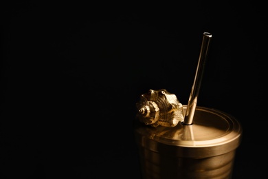 Photo of Gold cup with seashell on black background. Space for text