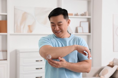 Photo of Handsome man applying body cream onto his elbow at home